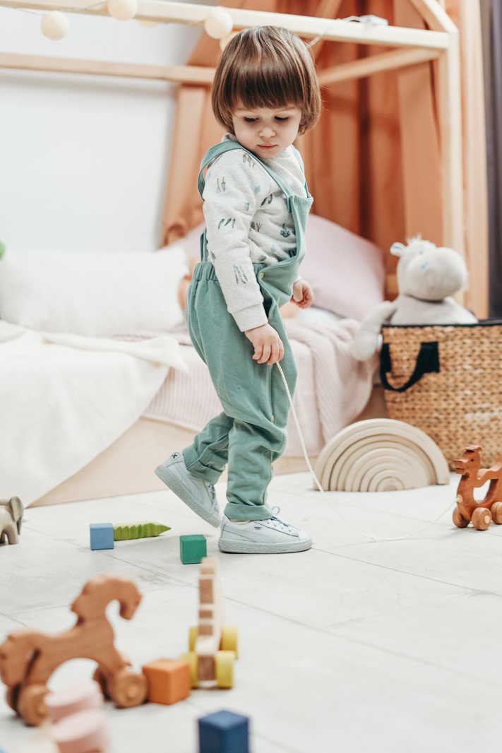 Child in White Long-sleeve Top and Green Dungaree Trousers Playing With Toys
